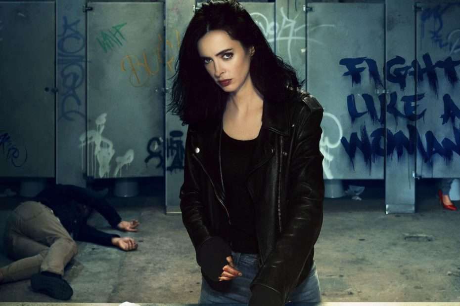 Jessica Jones con chaqueta de cuero en un baño lleno de grafitis, mensaje Fight like a woman en la pared