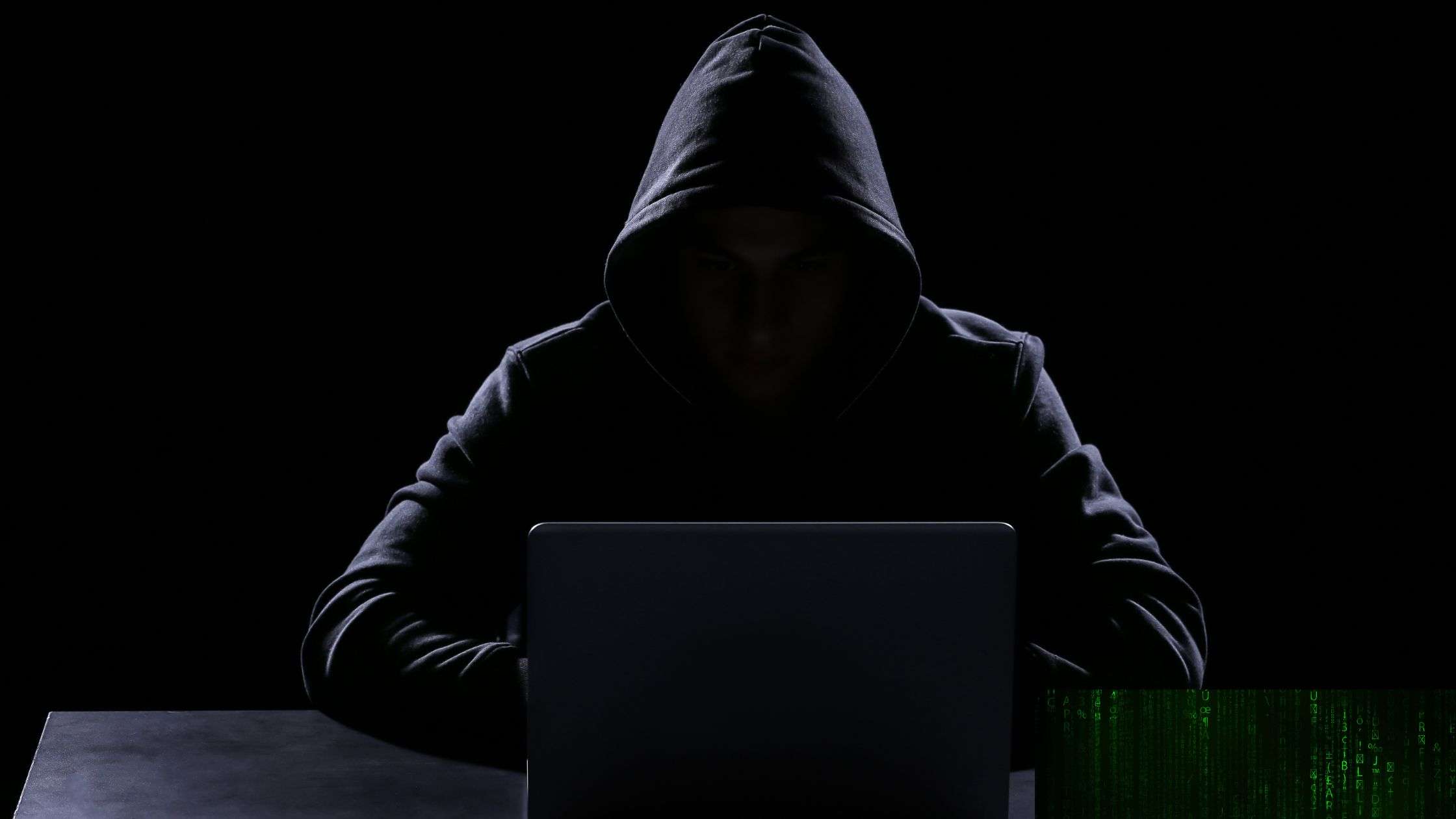 Silueta oscura de un hacker con capucha frente a un ordenador portátil, representando la figura del 'asesino invisible' en la novela negra contemporánea y el peligro del crimen digital.